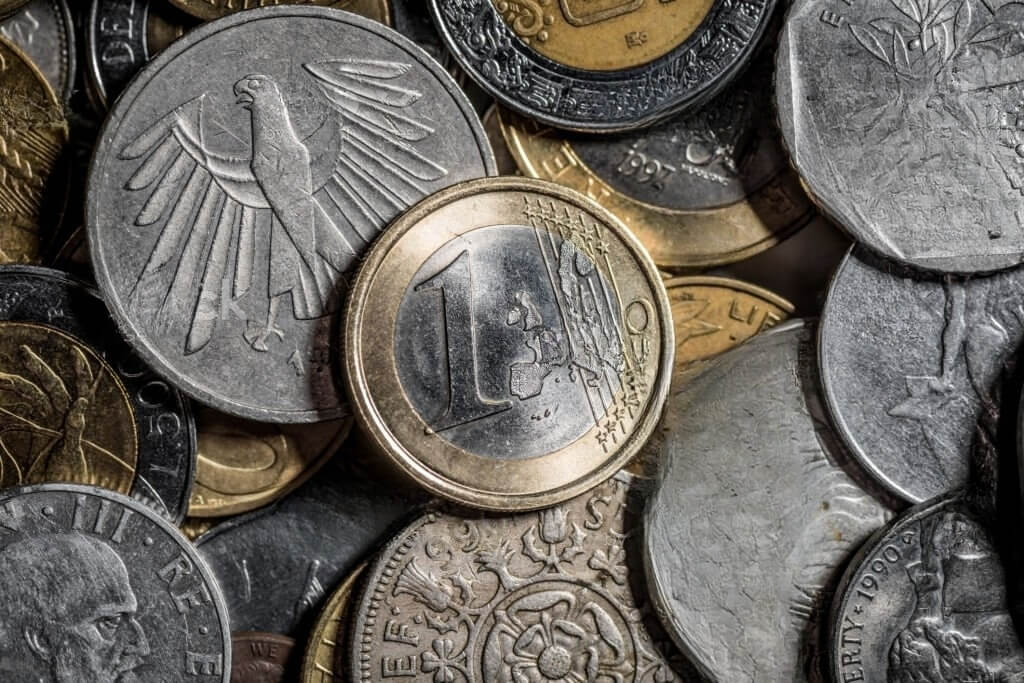 A one euro coin placed on top of a backdrop of various old currencies.